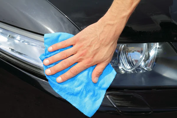 Car washing concept. Man cleaning car headlight with microfiber cloth