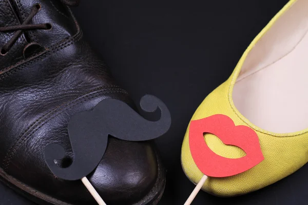 Amor, fondo de pareja feliz. Zapatos masculinos y femeninos con bigote divertido y labios en palos — Foto de Stock
