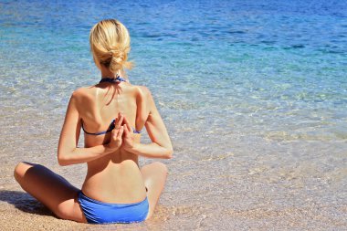 Sahilde yoga yapan genç bir kadın.