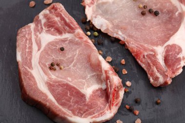 Siyah zemin üzerinde tuz ve biberli dilimlenmiş çiğ domuz eti.