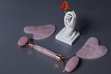 Gua Sha masaj aleti ve gri arka planda yeşim silindir. Yüz ve vücut bakımı için pembe yeşim taşı. Minimalist Estetik