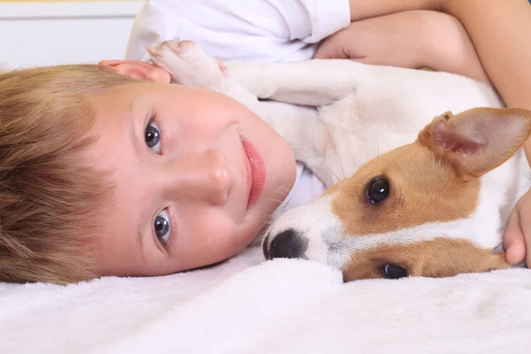 Joven abrazando su perro en la cama — Foto de Stock