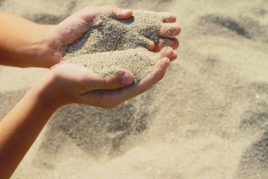 Close up on Childs hands holding sand. Sand flowing through the hands. Summer beach holiday vacation concept