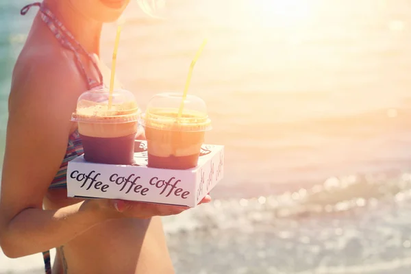 Aantrekkelijke vrouwelijke obers houden twee ijs frappe koffie op het strand in de buurt van zee, zonsondergang kleuren — Stockfoto