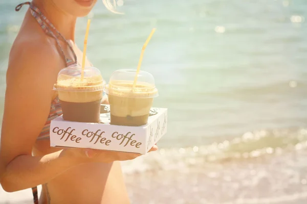 Atractivas mujeres sosteniendo dos frappe de hielo café en la playa cerca del mar — Foto de Stock
