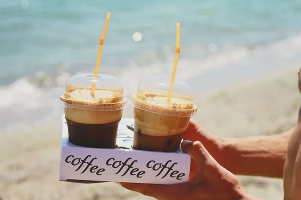 Manos masculinas sosteniendo dos frappe de hielo café en la playa cerca del mar — Foto de Stock