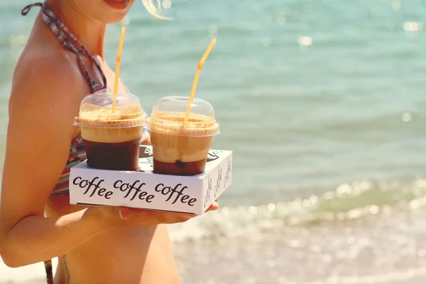 Atractivas mujeres sosteniendo dos frappe de hielo café en la playa cerca del mar — Foto de Stock