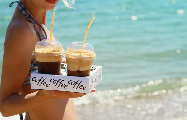 Attraktiva kvinnliga servitörer håller två ice frappe kaffe på stranden nära havet. Ung kvinna enjoyng under sommarsemester, semester på tropical resort vid hav. — Stockfoto