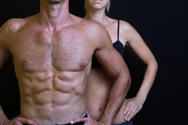 Musculação, desporto, fitness, conceito de treino. Fit casal, homem musculoso forte e mulher magra posando em um fundo preto — Fotografia de Stock