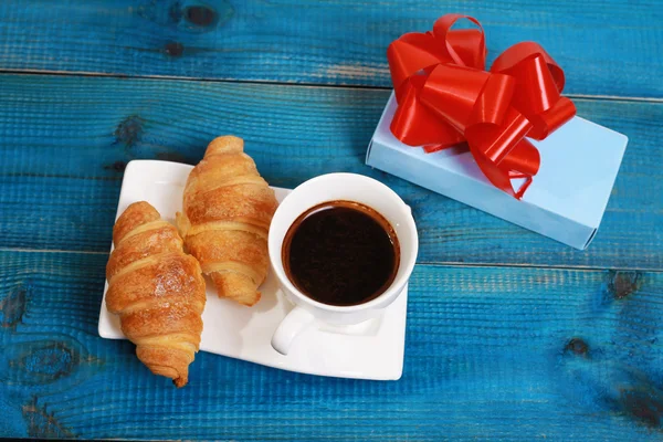 Taza de café, croissants y presente, regalo sobre fondo rústico azul de madera. Concepto romántico de desayuno de vacaciones —  Fotos de Stock