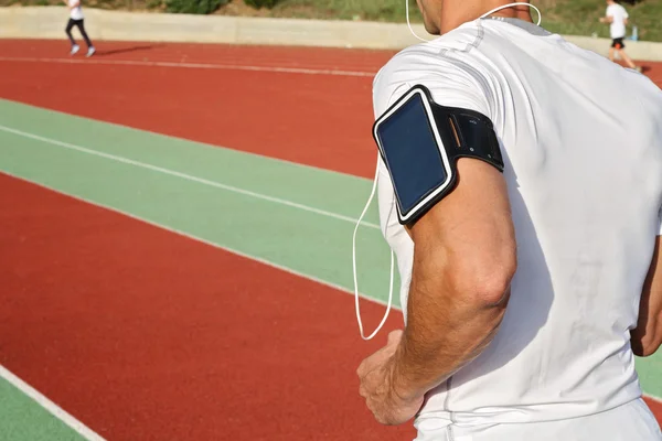 Man running down stadium track. Male runner  listening to music on mp3 player or mobile phone — Stock Photo, Image