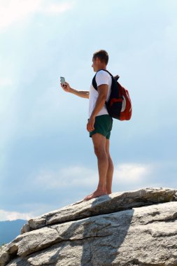 Young man with standing and taking selfie on top of a mountain