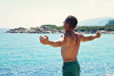 Man Raising His Hands or Open arms  looking to sea blue sky horizon. Strong muscular Men, perfect body, arms, back. Freedom Concept