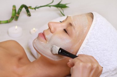 Kadın yüzünü yüz maskesi uygulayarak makyajcısı. Genç güzel kız yüz maskesi spa güzellik salonunda alma. Cilt Bakımı, güzellik uygulamaları.