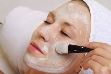 Kadın yüzünü yüz maskesi uygulayarak makyajcısı. Genç güzel kız yüz maskesi spa güzellik salonunda alma. Cilt Bakımı, güzellik uygulamaları.