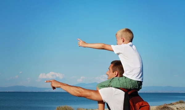 Vater gibt seinem Sohn Huckepack-Fahrt ins Freie. Mann und Sohn vor dem Meer, wegzeigen, aktiver Sommerurlaub, Familienreise Foto — Stockfoto