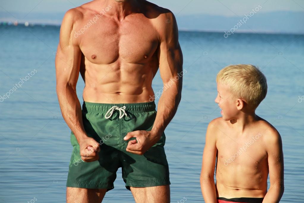 Father and son, boy and man showing muscles on the beach near sea