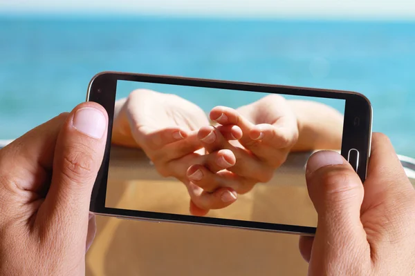 Mână de sex masculin luând fotografie pe mâinile femeilor care se bucură de vacanță de vară, vacanță cu celulă, telefon mobil. Femeie, relaxare, plajă, luând baie de soare, mare, ocean, paradis . — Fotografie, imagine de stoc