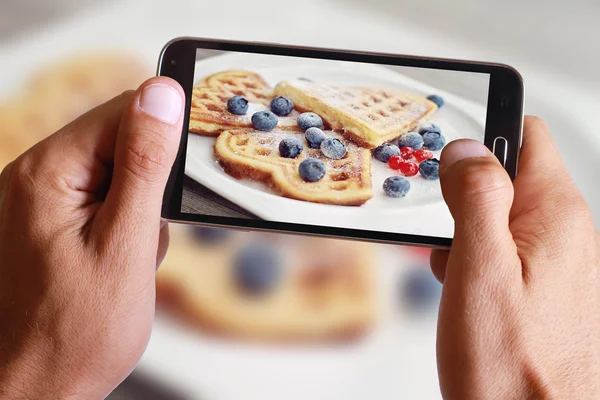 Male hand taking photo of waffles with blueberries with cell, mobile phone.