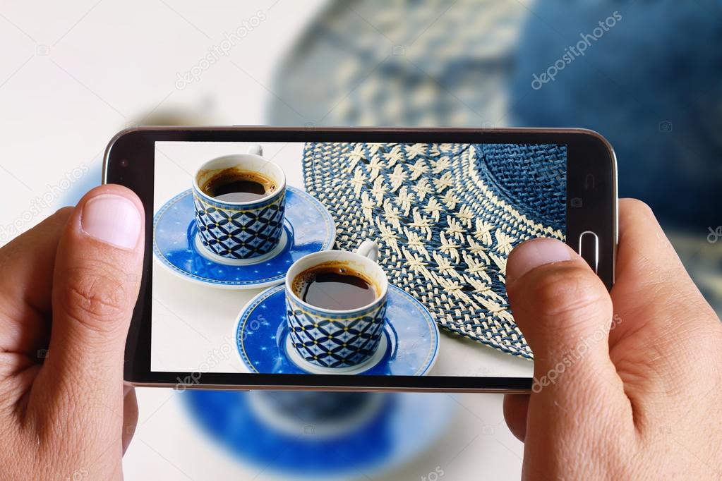 Male hand taking photo of Summer coffee break , female straw hat and two cups of home made coffee with cell, mobile phone.