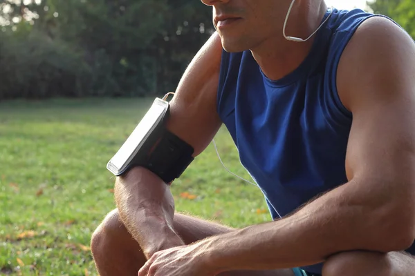 Male runner with mobile smart phone, listening to the music during workout. Athlete resting and relaxing after workout. Running, jogging, cardio, sport, active lifestyle concept