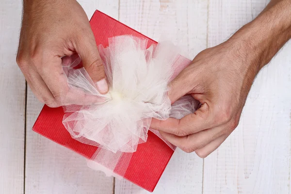 Nahaufnahme männlicher Hände mit rotem Geschenk und weißer Schleife. Geschenkverpackung. Geburtstag, Neujahr, Valentinstag, 8. März, Weihnachtskonzept. — Stockfoto