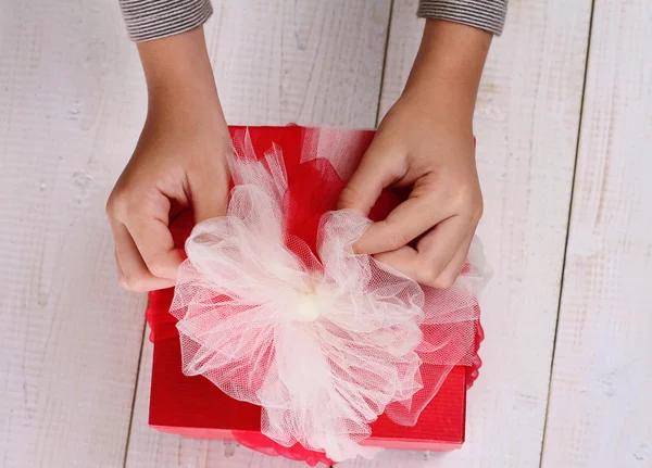 Close up on  child's  hands holding red present with white Ribbon . Gift box packaging. Birthday, New year, Christmas concept. — Stock Photo, Image