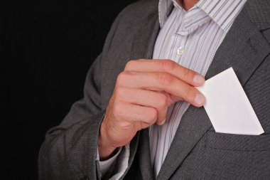 Business man putting a blank business card in his suit pocket. Closeup of a businessman taking a business card from the breast pocket of his suit jacket.