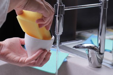 Close up of woman hands washing dishes by sponge, modern kitchen faucet and sink. House cleaning and home hygiene concept