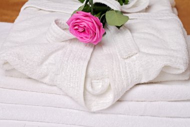 Stack of white  and soft hotel towels and bathrobe decorated with rose flower. Perfect white laundry. Spa, healthy lifestyle and relaxation concept.