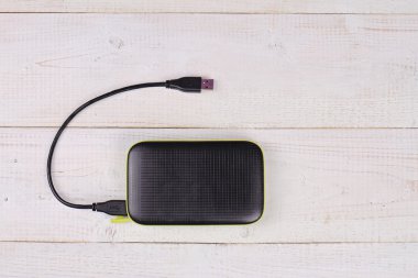 Portable external hard disk drive with USB cable on white wooden background. Copy space image