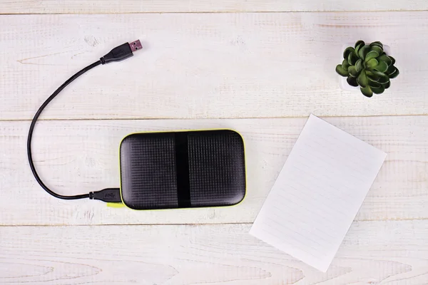 Portable external hard disk drive with USB cable  and blank message paper on white wooden background  Copy space image — Zdjęcie stockowe