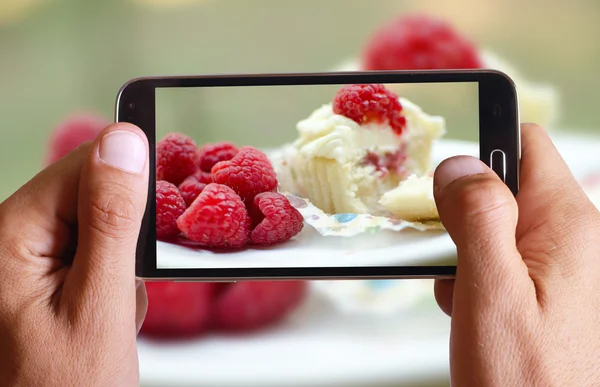 Male hand taking photo of vanilla ice cream with raspberry with cell, mobile phone.