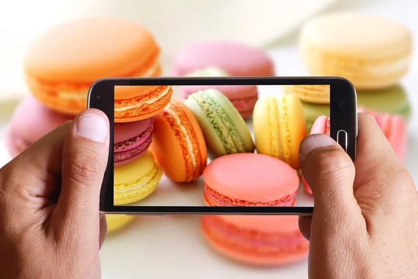 Male hand taking photo of macarons cakes with cell, mobile phone.