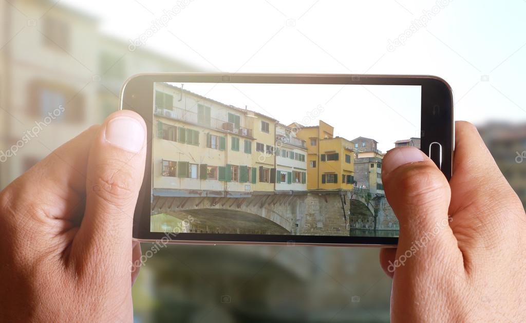 Male hand taking photo of Ponte Vecchio in Florence with cell, mobile phone.