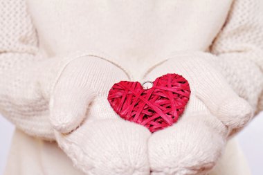 Female hands in white knitted cozy mittens holding heart shape christmas tree decoration. Love concept. Winter and Christmas time