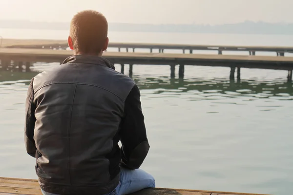 Hombre sentado en el viejo muelle de madera y mirando el horizonte del lago. Pensamiento, contemplación relajante, concentración, concepto de soledad — Foto de Stock