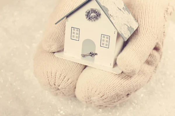 Female hands in white knitted cozy mittens holding cute house on — Stock Photo, Image