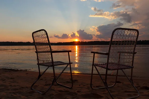 Sillas en la orilla del río contra el atardecer — Foto de Stock