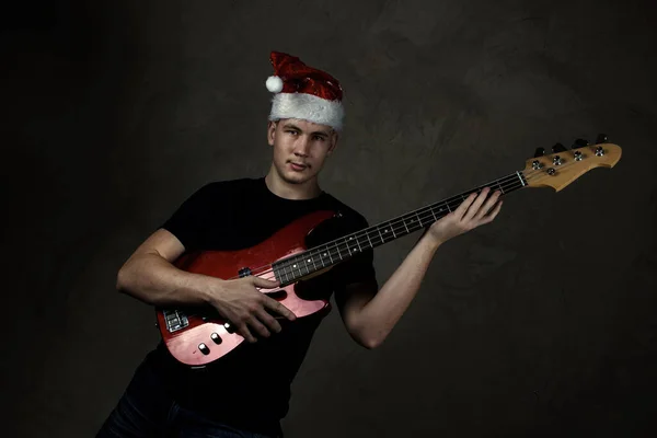 Jeune homme au bonnet de Nouvel An avec une guitare. Vacances. Fond gris — Photo