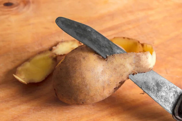 Rohe Kartoffeln schälen auf einem Holztisch. Wurzeln geschält und ungeschält neben Lebensmittelabfällen. Kochen. Selektiver Fokus. — Stockfoto