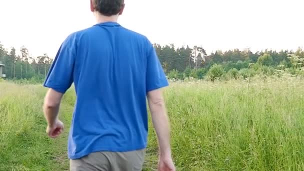 Чоловік, що йде по дорозі на полі в літній день — стокове відео