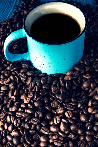 Schwarzer Kaffee im blauen Becher auf dem Tisch zwischen verstreuten Kaffeebohnen — Stockfoto