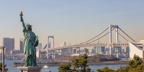 Lady liberty kontrasteras mot rainbow bridge i tokyo, japan. — Stockfoto