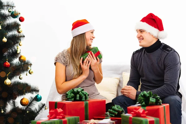 愛の贈り物を交換するカップルは 前景に赤と緑の包装紙 白の背景に贈り物の山は クリスマスツリーです ストックフォト