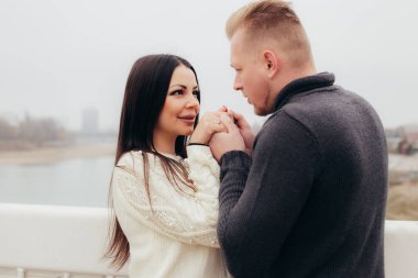 Bir erkek bir kadının elini tutar, gülümser ve sisli bir manzaranın arka planında birbirlerine bakarlar. Yüksek kalite fotoğraf