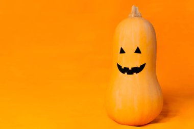 Cadılar Bayramı 'nda turuncu arka planda neşeli bir yüzü olan balkabağı.