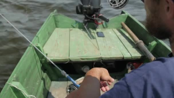 Un pêcheur attrape du poisson assis dans un bateau en bois. — Video