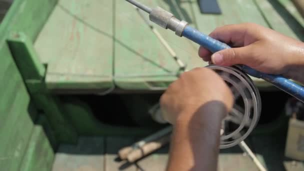 A fisherman catches fish sitting in a wooden boat. Close up shot of spinning — Vídeo de stock