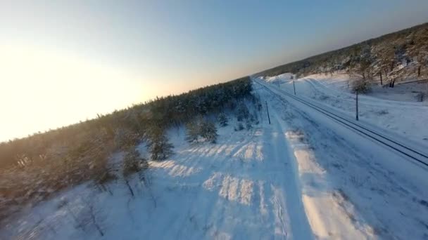 Widok drona FPV. Szybki lot nad koleją w zimowym lesie o zachodzie słońca — Wideo stockowe